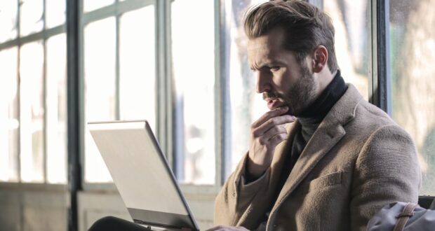 man holding his chin facing laptop computer