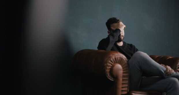a man holds his head while sitting on a sofa