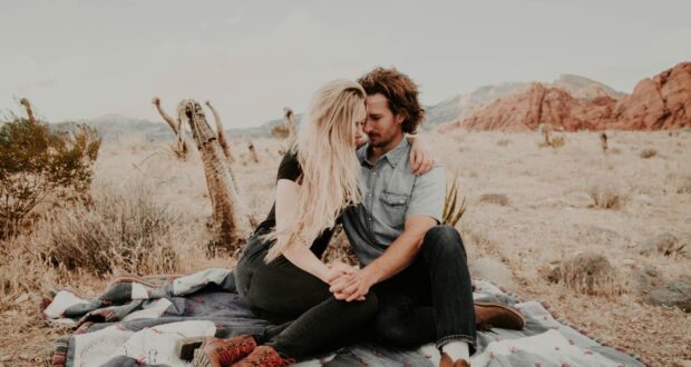 man and woman sitting on blanket while holding each other hands